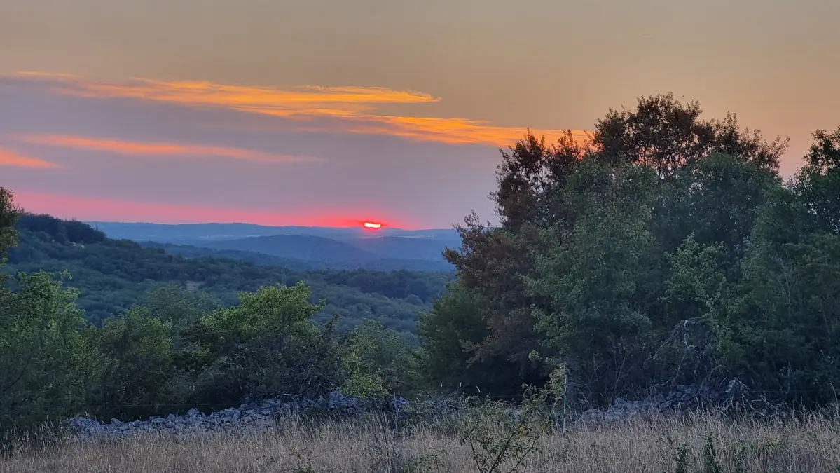 coucher de soleil sur le causse du Quercy en juin 26, on devine la silhouetter d'un arbre à droite au dessus d'un mur en pierres sèches, au loin les collines