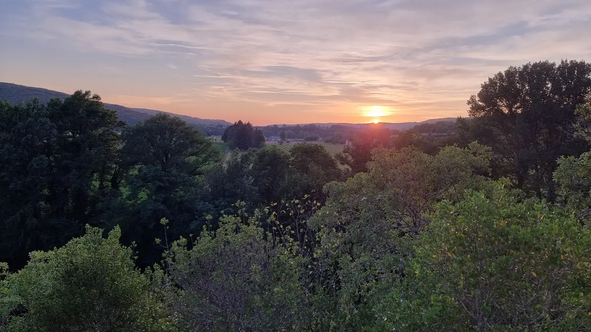 Coucher de soleil sur la vallée du Lot devant le village de Salvagnac Cajarc en août 26, on devine des champs derrrière les arbres